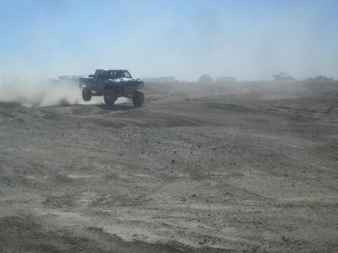 1990 Ford Bronco - Action photo of a blue off-road truck at speed on a desert course, not a technical document.