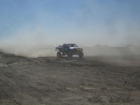 1990 Ford Bronco - Action photo of a blue off-road truck at speed with lights on, not a technical document.