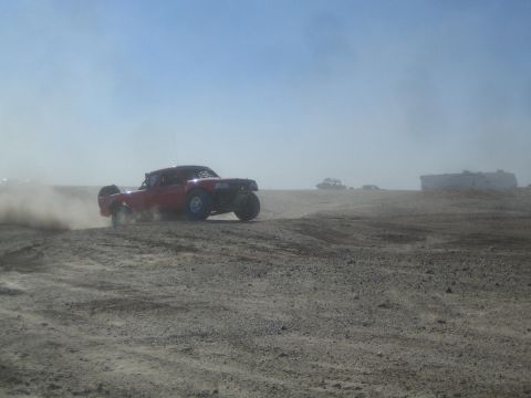 1990 Ford Bronco - Action photo of a red off-road truck at speed on a desert course, not a technical document.