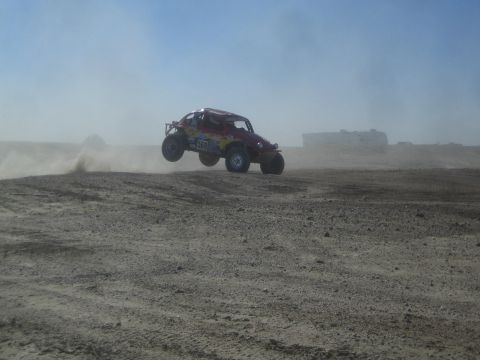 1990 Ford Bronco - Photograph of a brightly colored off-road race buggy airborne in a dusty desert, not a technical document.