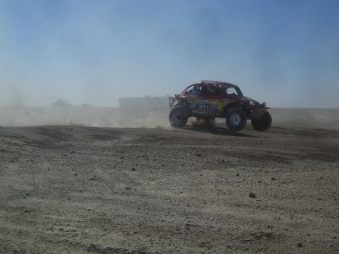1990 Ford Bronco - Photograph of a Baja-style off-road race buggy racing through desert dust, not a technical document.
