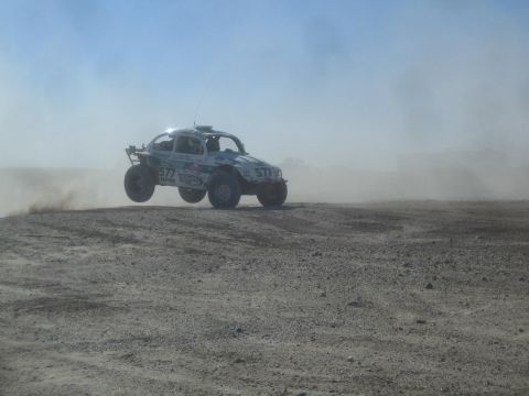 1990 Ford Bronco - Photograph of a white Baja Bug off-road racer airborne in blowing desert dust, not a technical document.