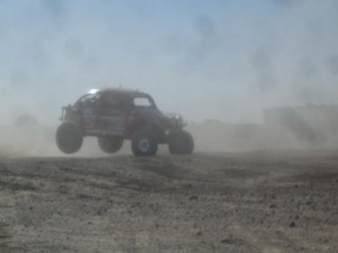1990 Ford Bronco - Blurry photograph of a red Baja Bug off-road racer airborne in desert dust, not a technical document.