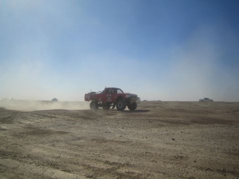 1990 Ford Bronco - Photograph of a red off-road race truck on an open dusty desert course, not a technical document.