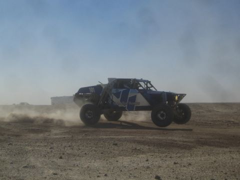 1990 Ford Bronco - Photograph of a blue sponsored off-road race truck racing through desert dust, not a technical document.