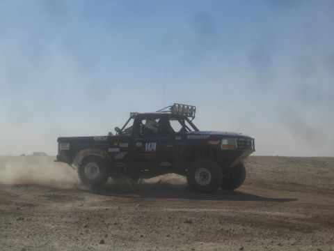 1990 Ford Bronco - Photograph of a black off-road race truck with a roof light bar racing in the desert, not a technical document.