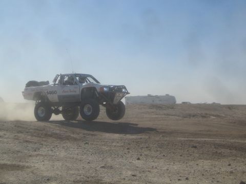 1990 Ford Bronco - Photograph of a white off-road race truck jumping in a dusty desert, not a technical document.