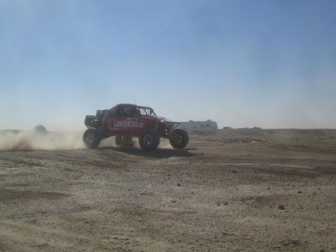 1990 Ford Bronco - Photograph of a red sponsored off-road race truck racing through desert dust, not a technical document.