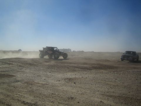 1990 Ford Bronco - Photograph of an off-road race truck and a chase vehicle in a dusty desert, not a technical document.