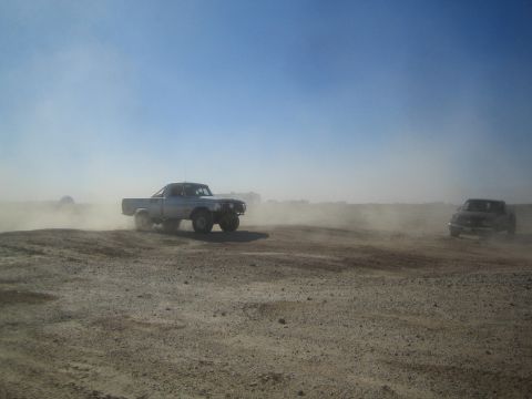 1990 Ford Bronco - Photograph of a silver pickup off-road racer on a dusty desert course, not a technical document.