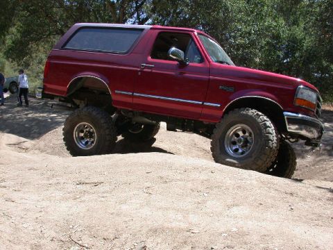 1996 Ford Bronco - Red 1992-96 Ford Bronco flexing over a dirt mound at an off-road park, shown from the passenger side with the front tire climbing and the r…