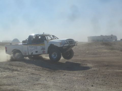 1990 Ford Bronco - Photograph of a white sponsored off-road race truck airborne in a dusty desert, not a technical document.