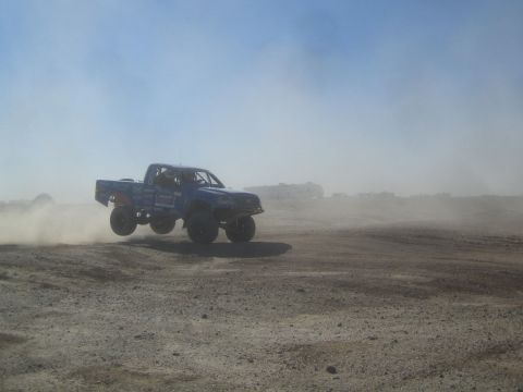1990 Ford Bronco - Photograph of a blue off-road race truck jumping in a dusty desert, not a technical document.