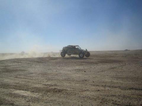 1990 Ford Bronco - Action photo of an off-road tube-frame buggy racing across a dusty desert track, not a technical document.