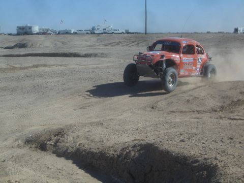 1990 Ford Bronco - Action photo of an orange Baja Bug racing through dust on a desert course, not a technical document.