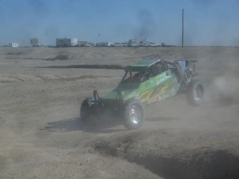 1990 Ford Bronco - Action photo of a green off-road tube-frame buggy sliding through dust on a desert track, not a technical document.