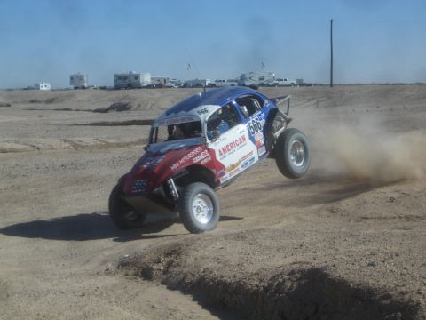 1990 Ford Bronco - Action photo of a red, white and blue Baja Bug number 566 racing through dust on a desert course, not a technical document.