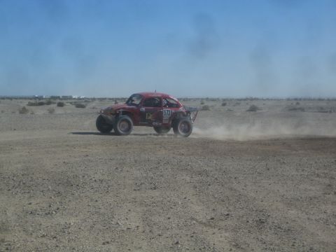 1990 Ford Bronco - Action photo of a red Baja Bug racing through dust on a flat desert course, not a technical document.