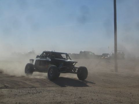 1990 Ford Bronco - Action photo of a black off-road buggy racing through heavy dust on a desert course, not a technical document.