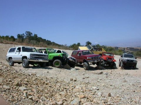 1996 Ford Bronco - A row of lifted 4x4s parked side by side on a rocky hilltop staging area under clear blue sky, including a white square-body Chevy/GMC K5-s…