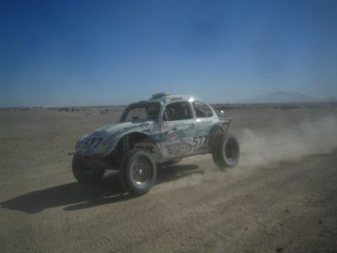 1990 Ford Bronco - Action photo of a white Class 5 Baja Bug (number 577) racing across a dusty desert track; not a technical document.