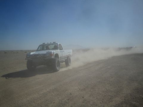 1990 Ford Bronco - Action photo of a white off-road race pickup trailing dust on a desert course; not a technical document.