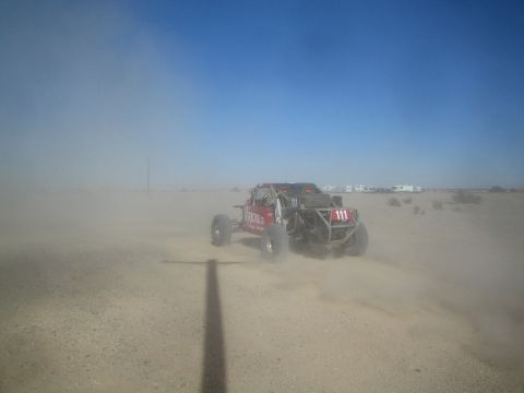 1990 Ford Bronco - Action photo of a red off-road buggy (number 111) racing through heavy desert dust; not a technical document.