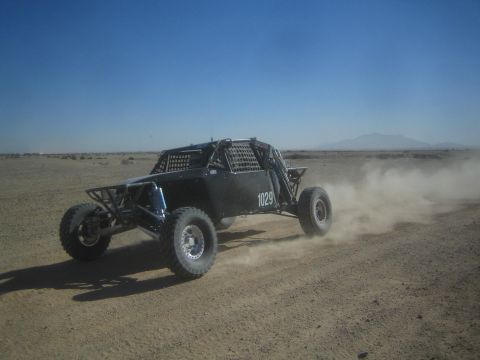 1990 Ford Bronco - Action photo of a black tube-frame off-road buggy (number 1029) racing on a desert track; not a technical document.