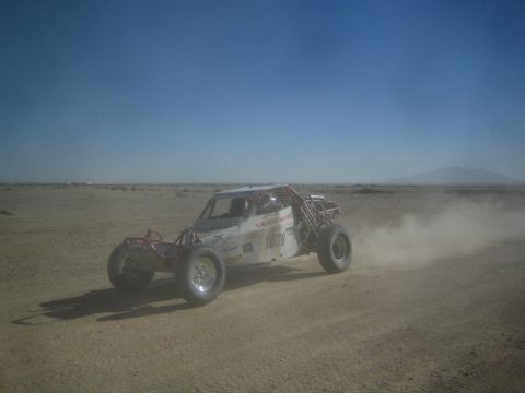 1990 Ford Bronco - Action photo of a white off-road race buggy speeding through desert dust; not a technical document.