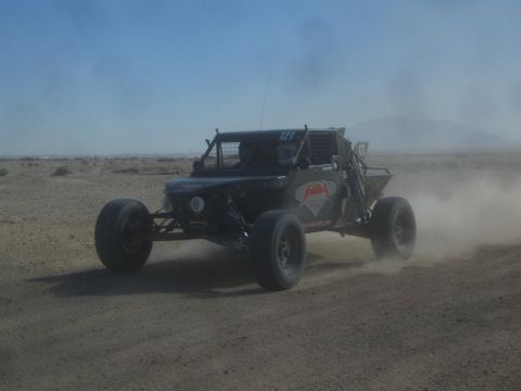 1990 Ford Bronco - Action photo of a black off-road buggy (number 121) racing through desert dust; not a technical document.
