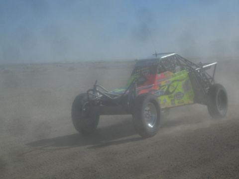 1990 Ford Bronco - Action photo of a brightly painted off-road race buggy speeding through desert dust; not a technical document.