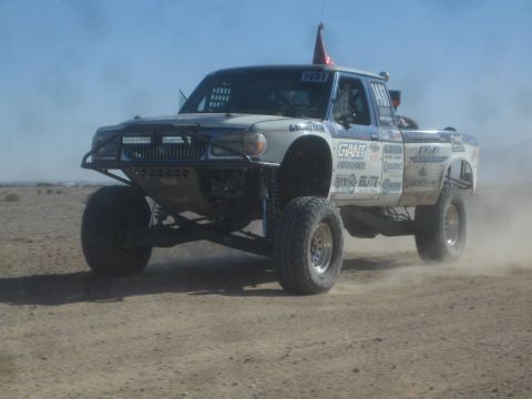 1990 Ford Bronco - Action photo of a silver sponsor-decaled off-road race truck (number 1451) on a desert course; not a technical document.