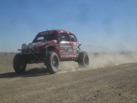 1990 Ford Bronco - Action photo of a red Baja Bug with roof lights racing through desert dust; not a technical document.