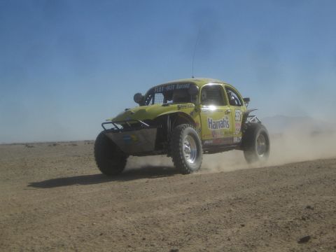 1990 Ford Bronco - Action photo of a yellow Flat-Out Racing Baja Bug racing across a desert track; not a technical document.