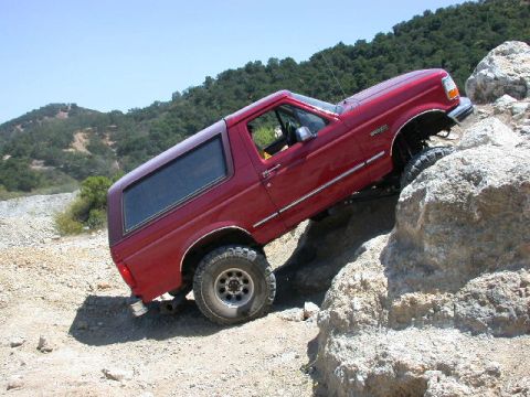 1996 Ford Bronco - Red 1992-96 Ford Bronco climbing a light-colored rock outcrop at a steep nose-up angle, photographed from the passenger side rear. The remo…