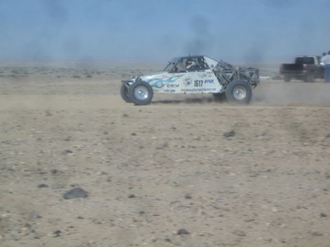 1990 Ford Bronco - Action photo of a white off-road buggy (number 1617) racing across a rocky desert flat; not a technical document.