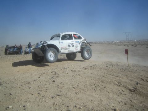 1990 Ford Bronco - Action photo of a white Baja Bug (number 576) cresting a rise on a desert course with spectators; not a technical document.