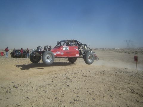 1990 Ford Bronco - Action photo of a red off-road buggy (number 1213) racing over a desert berm; not a technical document.