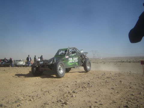 1990 Ford Bronco - Action photo of a green off-road buggy with a For Sale decal racing over a desert rise; not a technical document.