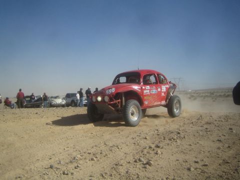 1990 Ford Bronco - Action photo of a red Baja Bug (number 596) on a desert course with spectators and chase vehicles; not a technical document.