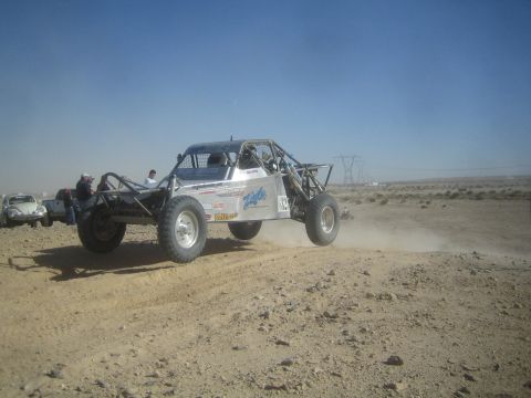 1990 Ford Bronco - Action photo of a white off-road race buggy launching off a desert berm near spectators; not a technical document.