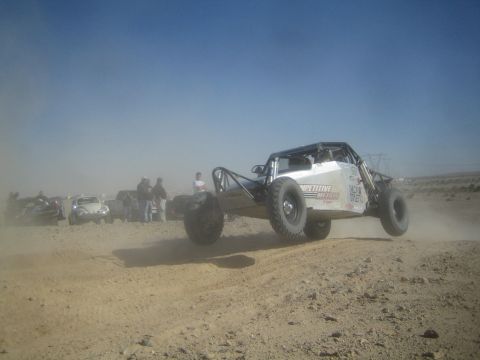 1990 Ford Bronco - Photograph of a white tube-chassis off-road race buggy catching air on a dusty desert race course.