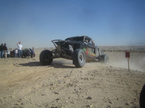 1990 Ford Bronco - Photograph of a black off-road race buggy driving past a course marker in the desert.