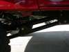 1996 Ford Bronco - Very small, low-resolution thumbnail looking under the rear of a red vehicle, showing a dark suspension and axle area above a light concret…