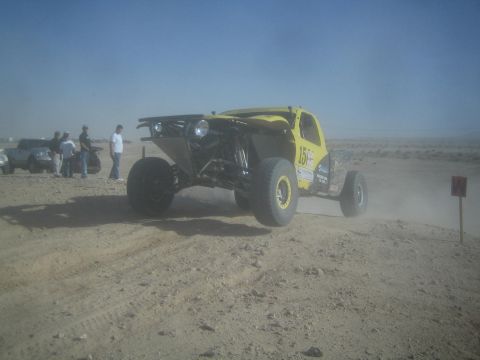 1990 Ford Bronco - Photograph of a yellow tube-chassis off-road race buggy driving on a desert race course with onlookers.