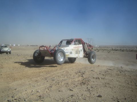 1990 Ford Bronco - white and red single-seat off-road race buggy numbered 1620 runs across a dusty desert course with power lines on the horizon.