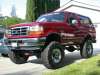 1996 Ford Bronco - A dark red/maroon Ford Bronco full-size SUV shown from a front three-quarter angle, heavily lifted on large off-road tires with a white rem…