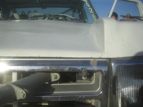 1990 Ford Bronco - close-up detail of a white off-road truck showing its hood seam, chrome grille trim, and windshield wiper area under blue sky.