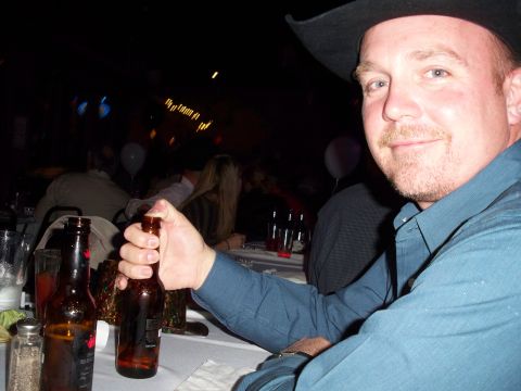 1996 Ford Bronco - A man wearing a cowboy hat is holding a beer bottle at a table with other people in the background.