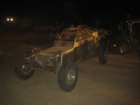1990 Ford Bronco - tube-chassis off-road sand rail buggy with large rear tires sits on packed dirt at night near other vehicles.